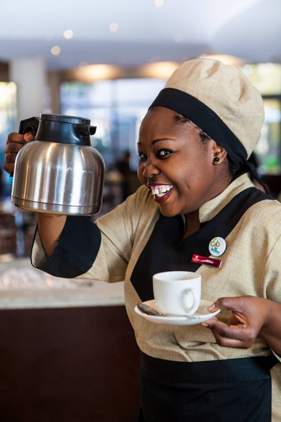 Photo of a smiling hotel staff member with a coffee pot and cup in her hands. NightOwl Media, Corporate Photography. Photographer based in Pretoria & Johannesburg, Gauteng, South Africa. Videographer, Marketing, Incentive, travel, lodge, corporate